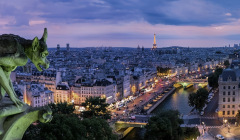 Blick über Paris bei Nacht, mit einem Wasserspeier der Kathedrale Notre-Dame im Vordergrund und dem beleuchteten Eiffelturm im Hintergrund.